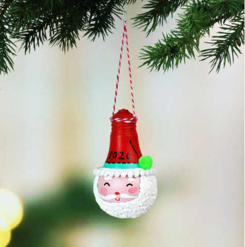 An Santa Claus ornament made from a recycled light bulb hangs off a Christmas tree.